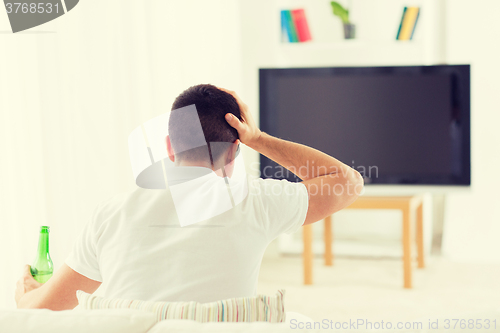 Image of man watching tv and drinking beer at home