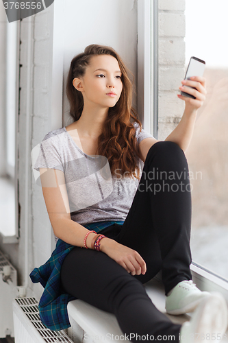 Image of sad pretty teenage girl with smartphone texting