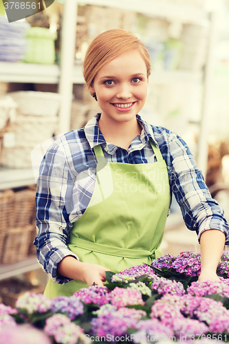 Image of happy woman taking care of flowers in greenhouse