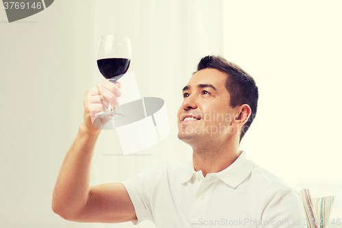 Image of happy man drinking red wine from glass at home