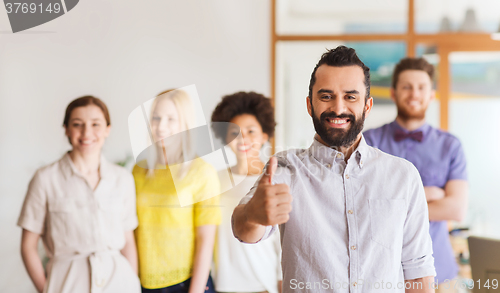 Image of happy man showing thumbs up over team in office