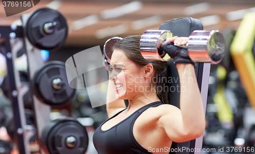 Image of young woman flexing muscles with dumbbell in gym