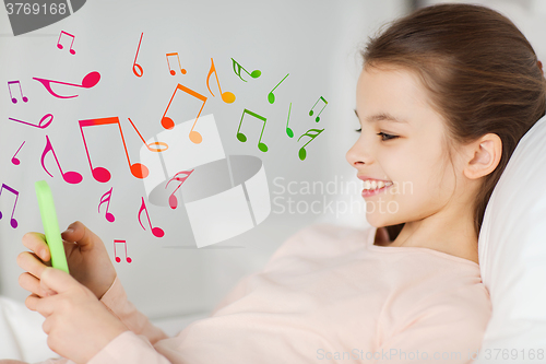 Image of happy girl lying in bed with smartphone over notes