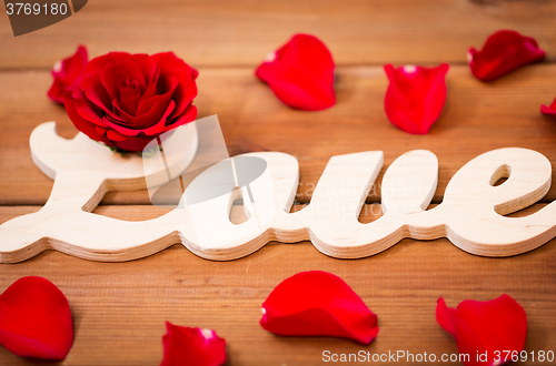 Image of close up of word love cutout with red rose on wood