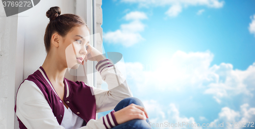 Image of sad pretty teenage girl sitting on windowsill