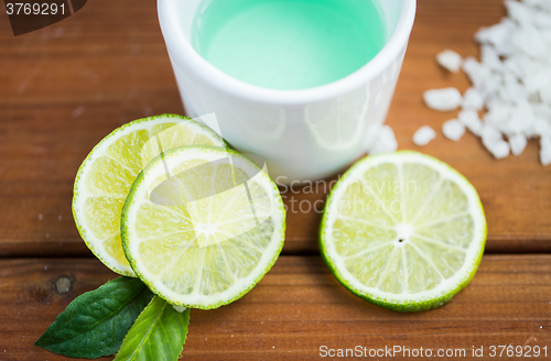 Image of close up of body lotion in cup and limes on wood
