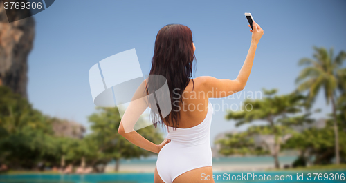 Image of young woman taking selfie with smartphone on beach