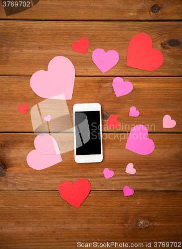 Image of close up of smartphone and hearts on wood