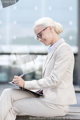 Image of young smiling businesswoman with notepad outdoors