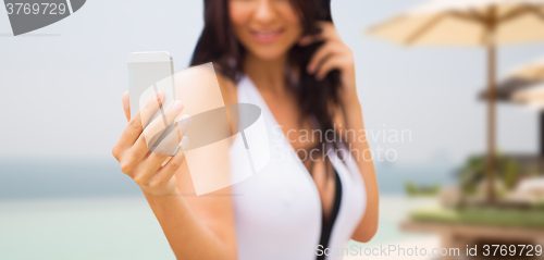 Image of young woman taking selfie with smartphone on beach