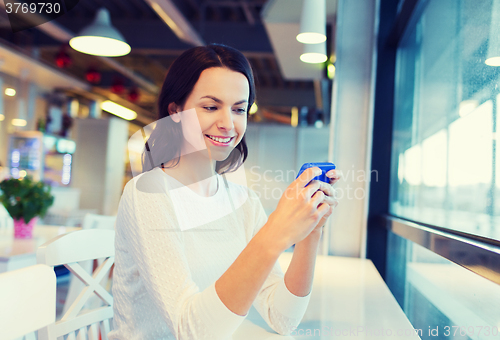 Image of smiling woman with smartphone at cafe
