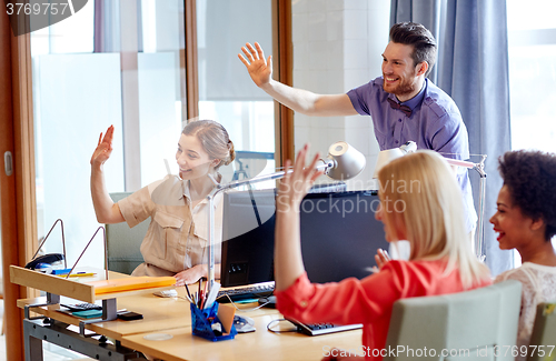 Image of happy creative team waving hands in office
