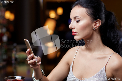 Image of young woman with smartphone at night club or bar