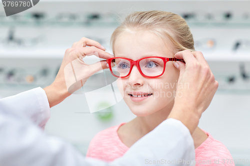 Image of optician putting glasses to girl at optics store