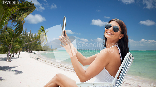 Image of smiling woman with tablet pc sunbathing on beach