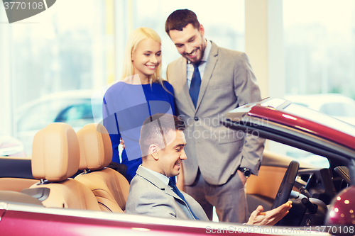 Image of happy couple with car dealer in auto show or salon