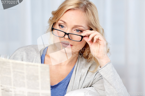 Image of woman in eyeglasses reading newspaper at home