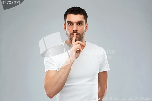 Image of young man making hush sign over gray background