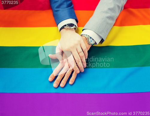 Image of close up of male gay couple hands on rainbow flag