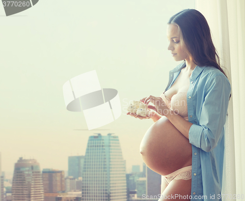 Image of happy pregnant woman with baby booties at home