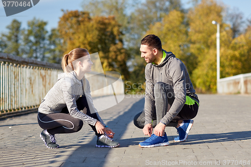 Image of smiling couple tying shoelaces outdoors