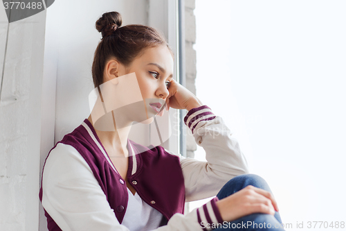 Image of sad pretty teenage girl sitting on windowsill