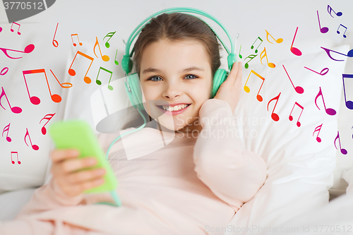 Image of happy girl in bed with smartphone and headphones