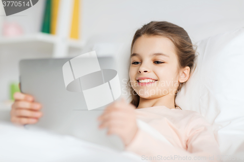 Image of happy girl lying in bed with tablet pc at home