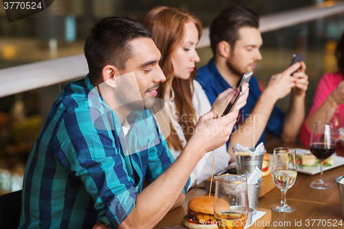 Image of friends with smartphones dining at restaurant