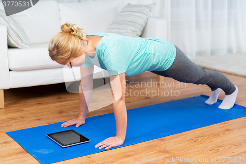 Image of woman with tablet pc doing plank exercise at home