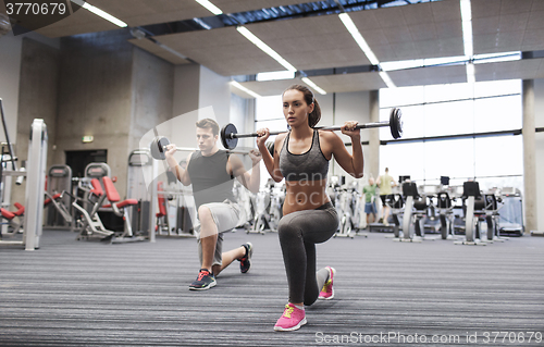 Image of young man and woman training with barbell in gym