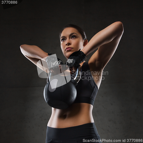 Image of young woman flexing muscles with kettlebell in gym