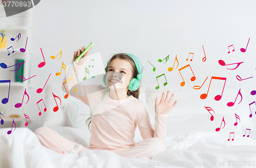 Image of girl sitting on bed with smartphone and headphones