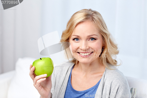 Image of happy middle aged woman with green apple at home