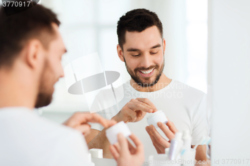 Image of happy young man applying cream to face at bathroom