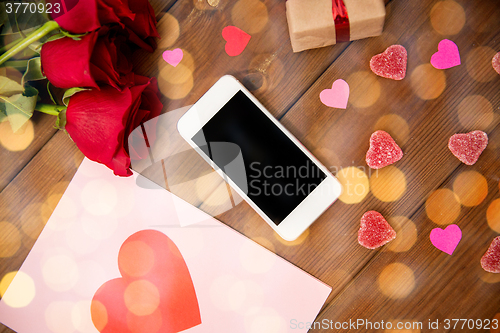 Image of close up of smartphone, gift, red roses and hearts