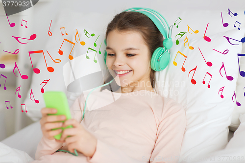 Image of happy girl in bed with smartphone and headphones