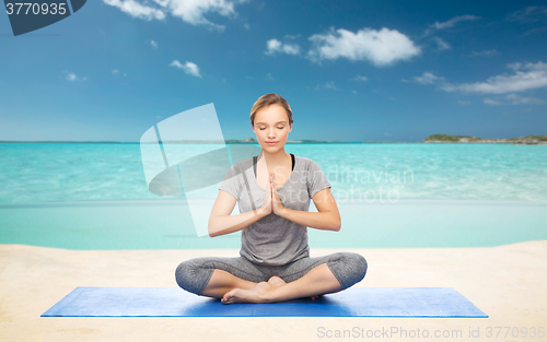 Image of woman meditating in lotus yoga pose on beach 