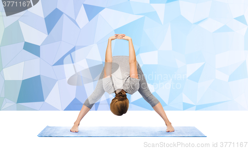 Image of woman making yoga wide-legged forward bend on mat