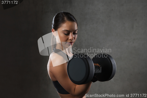 Image of young woman flexing muscles with dumbbells in gym