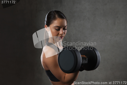 Image of young woman flexing muscles with dumbbells in gym