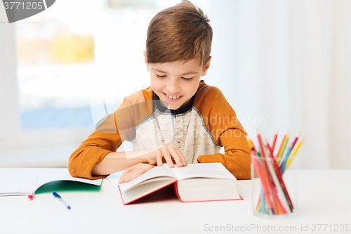 Image of smiling, student boy reading book at home