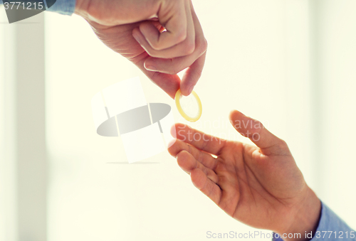 Image of close up of male gay couple hands giving condom