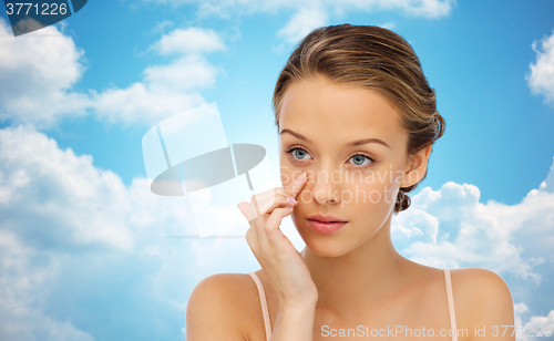 Image of young woman applying cream to face over blue sky