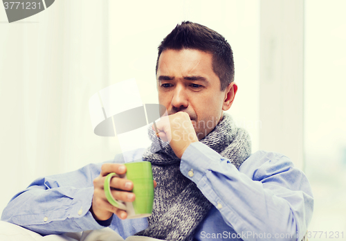 Image of ill man with flu drinking tea and coughing at home