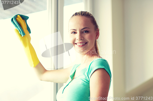 Image of happy woman in gloves cleaning window with rag