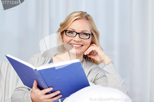 Image of smiling woman reading book and sitting on couch