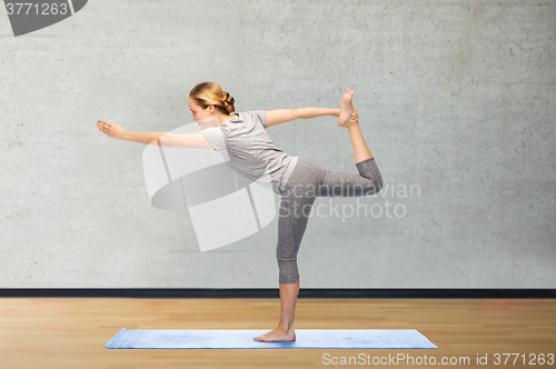 Image of woman making yoga in lord of the dance pose on mat