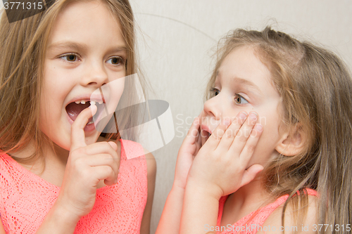 Image of Six year old girl shows her sister a four wobbly front tooth milk