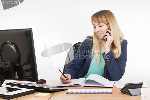 Image of Business woman talking on the phone and writes in the book office
